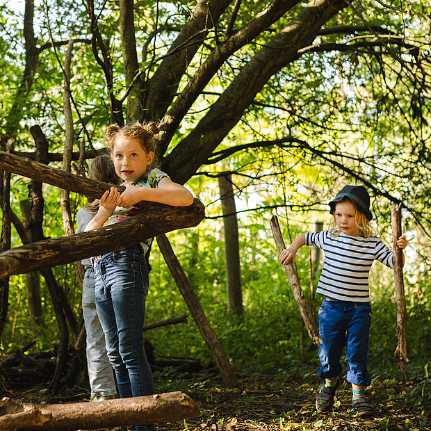 Kinder bauen mit Holzstämmen und -ästen ein Tipi im Naturerfahrungsraum Kienbergpark