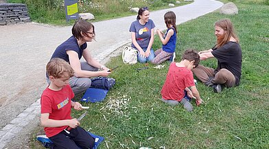 Auch im Schnitzen mit dem Naturprodukt Holz wurde sich beim 1. Naturentdeckertag im Kienbergpark mit dem Campus Stadt Natur ausprobiert, wie diese junge Familie auf der Wiese. 