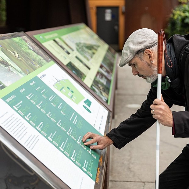 Eine blinde Person ertastet die Ausstellungstafeln der barrierefreien Ausstellung "Bahnbrechende Natur" im Natur-Park Schöneberger Südgelände