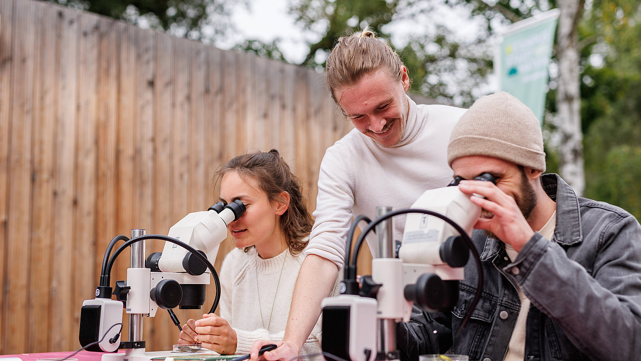 Zwei Erwachsene schauen mit Hilfe eines Workshop-Leiters durch Mikroskope
